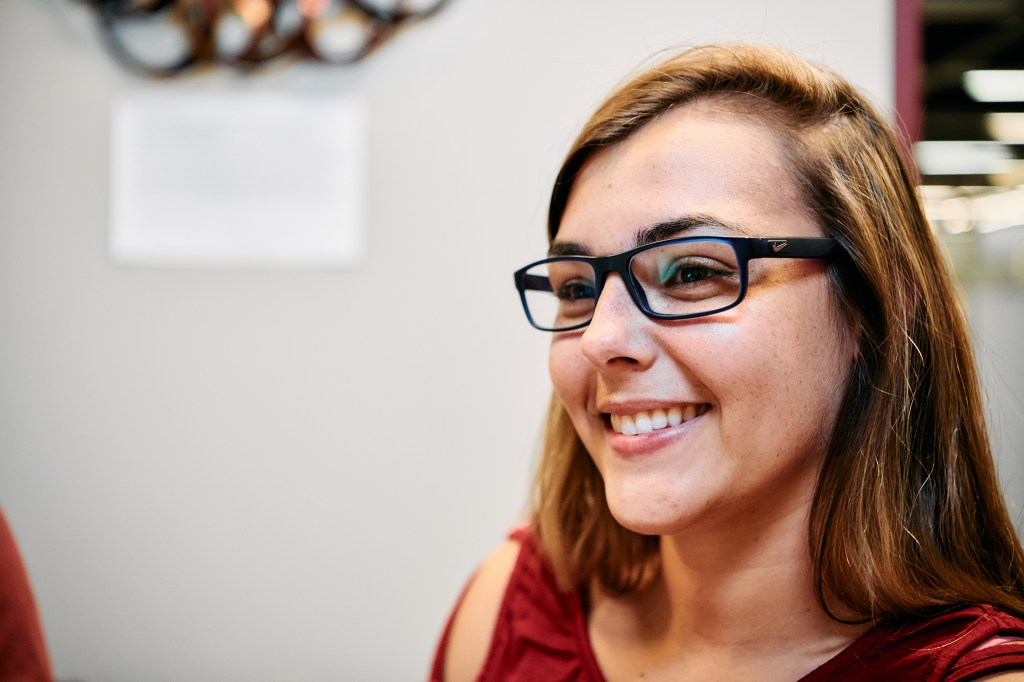 corner-clip A young woman wearing glasses sitting in an office environment.